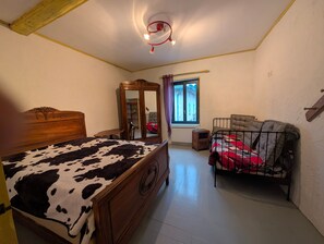 A bedroom with a wooden bed, a small bedside table, a wardrobe, a window with curtains, and a crib. - Apartment "Gîte Chez Mémé" with Wi-Fi (Assieu)