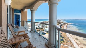 Un balcone con vista sulla spiaggia e sull'oceano, con due sedie di legno e una porta in vetro.