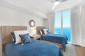 A hotel room with two beds, a ceiling fan, a large window with curtains, and a decorative mirror on the wall. - 🌴Luxury High-Rise w/Gulf + Sound Views + Resort Amenities | Portofino 4-1908 (Pensacola Beach)