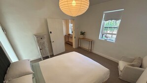 Un dormitorio con cama, mesita de noche, silla, armario y ventana con vistas al exterior.