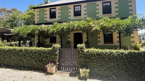 Una casa de dos pisos con fachada verde y beige, un portón de madera y un seto bien cuidado al frente.