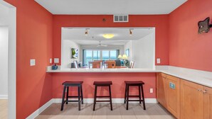 A kitchen with a red accent wall, white countertops, and three wooden stools. - ☀Stunning Beachfront Condo🐬Price Drop!🌴Private Balcony (Indian Rocks Beach)