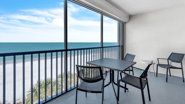 A balcony with a table and chairs, overlooking a beach and ocean. - ☀Stunning Beachfront Condo🐬Price Drop!🌴Private Balcony (Indian Rocks Beach)