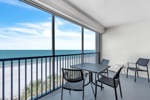 Un balcone con tavolo e sedie, vista sulla spiaggia e l'oceano.