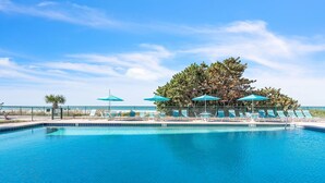A swimming pool with lounge chairs and umbrellas, surrounded by a fence and trees. - ☀Stunning Beachfront Condo🐬Price Drop!🌴Private Balcony (Indian Rocks Beach)