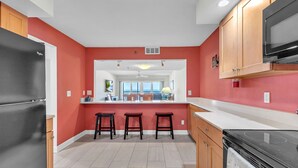 A modern kitchen with a red accent wall, a black refrigerator, wooden cabinets, and a black stove. - ☀Stunning Beachfront Condo🐬Price Drop!🌴Private Balcony (Indian Rocks Beach)