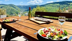 Una mesa de madera con una ensalada, una botella de vino y una copa de vino, con una vista panorámica de montañas al fondo.