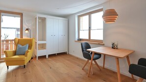 A modern living room with a yellow armchair, a wooden dining table, and a white cabinet. - New & high-quality furnished guest house in a quiet location - Burgberg im Allgäu (Burgberg im Allgäu)