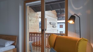 A room with a wooden bed, a yellow armchair, and a view of a wooden cabin through a glass door. - New & high-quality furnished guest house in a quiet location - Burgberg im Allgäu (Burgberg im Allgäu)