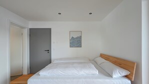 A bedroom with a wooden bed, white bedding, a gray door, and a framed artwork on the wall. - New & high-quality furnished guest house in a quiet location - Burgberg im Allgäu (Burgberg im Allgäu)
