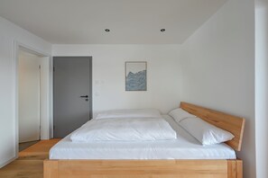 Ein Schlafzimmer mit einem hölzernen Bett, weißer Bettwäsche, einer grauen Tür und einem gerahmten Kunstwerk an der Wand.