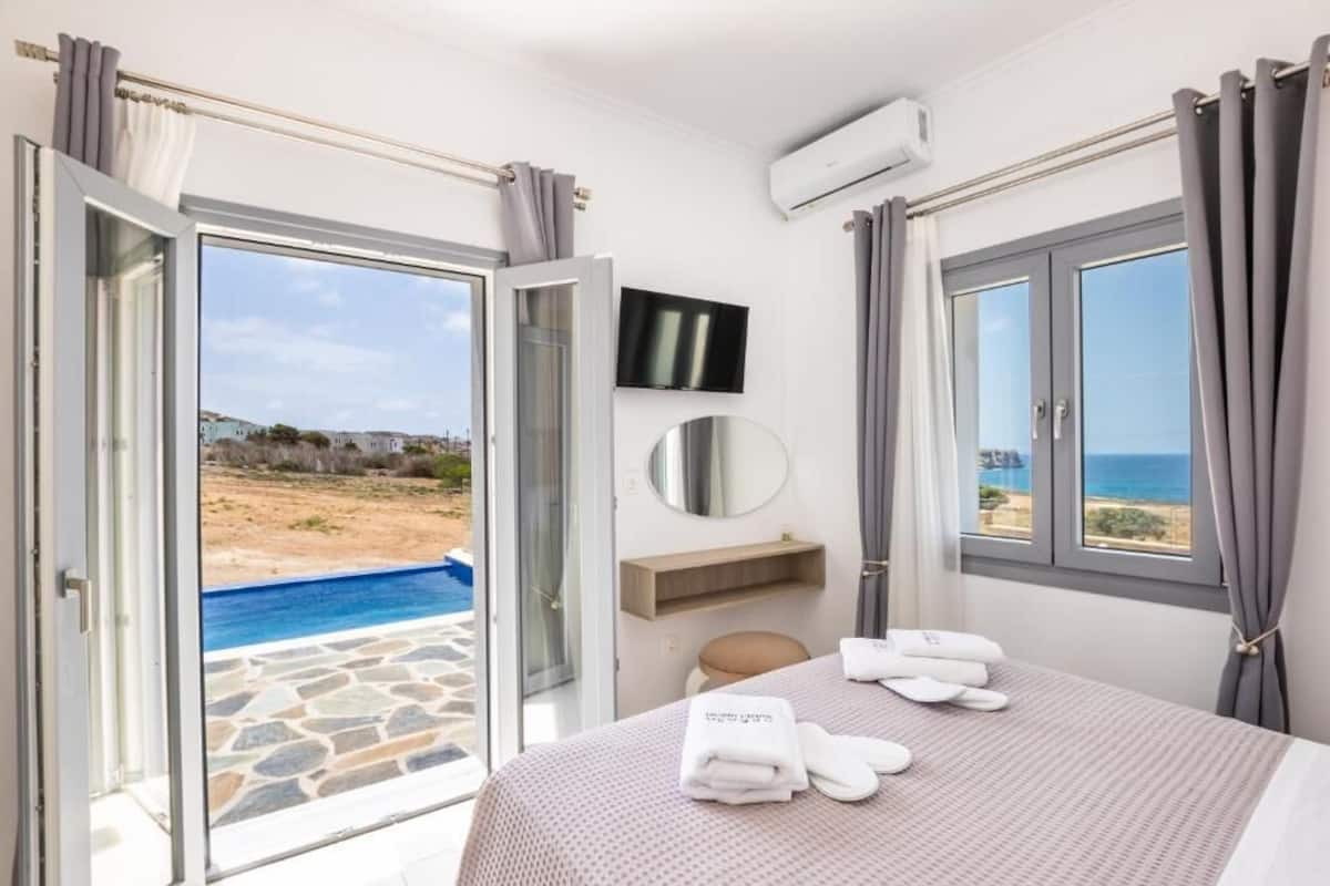 Un dormitorio con cama, televisor, espejo y vista a una piscina y una playa.