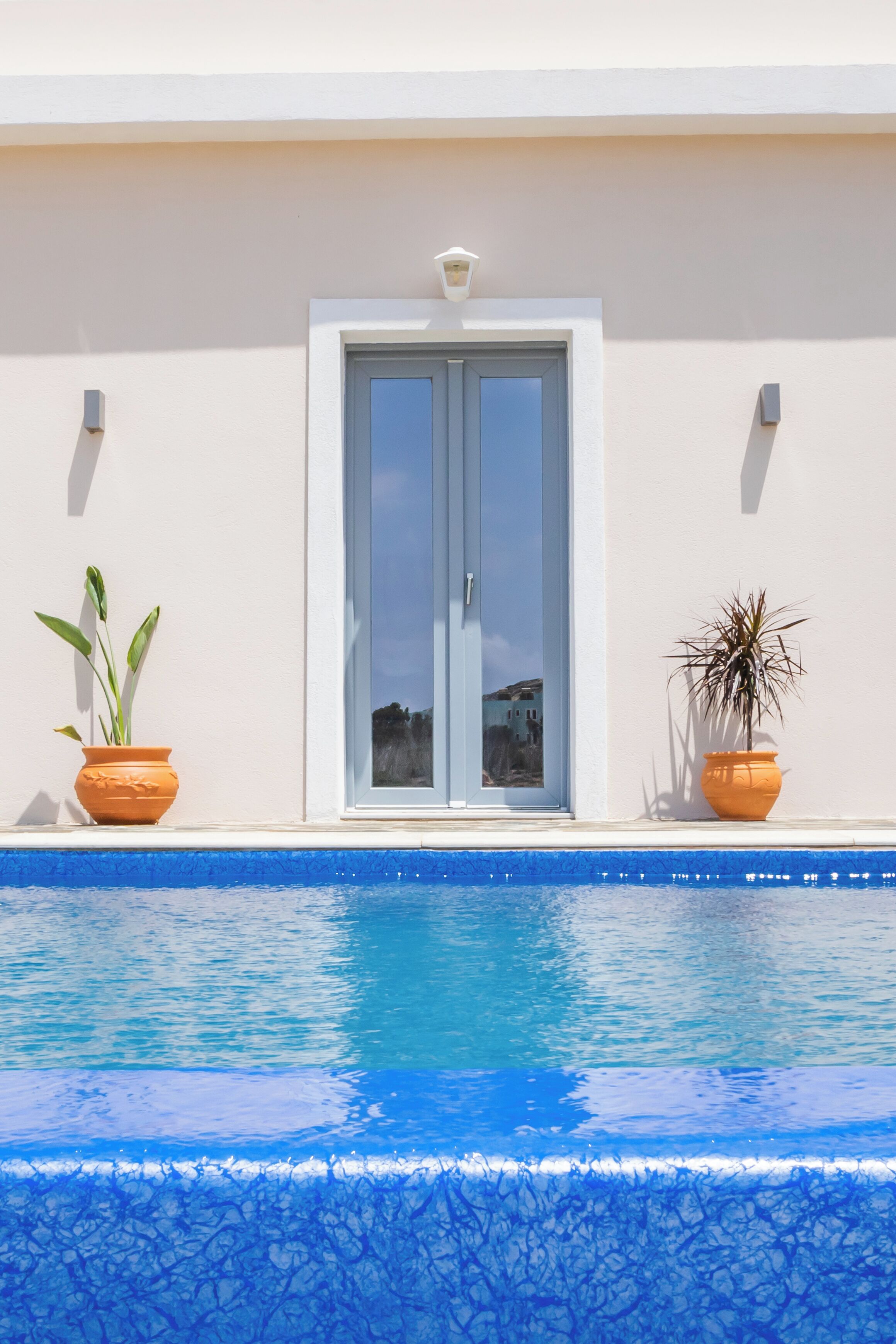 A swimming pool with a clear blue edge, a white door, and two potted plants on either side.