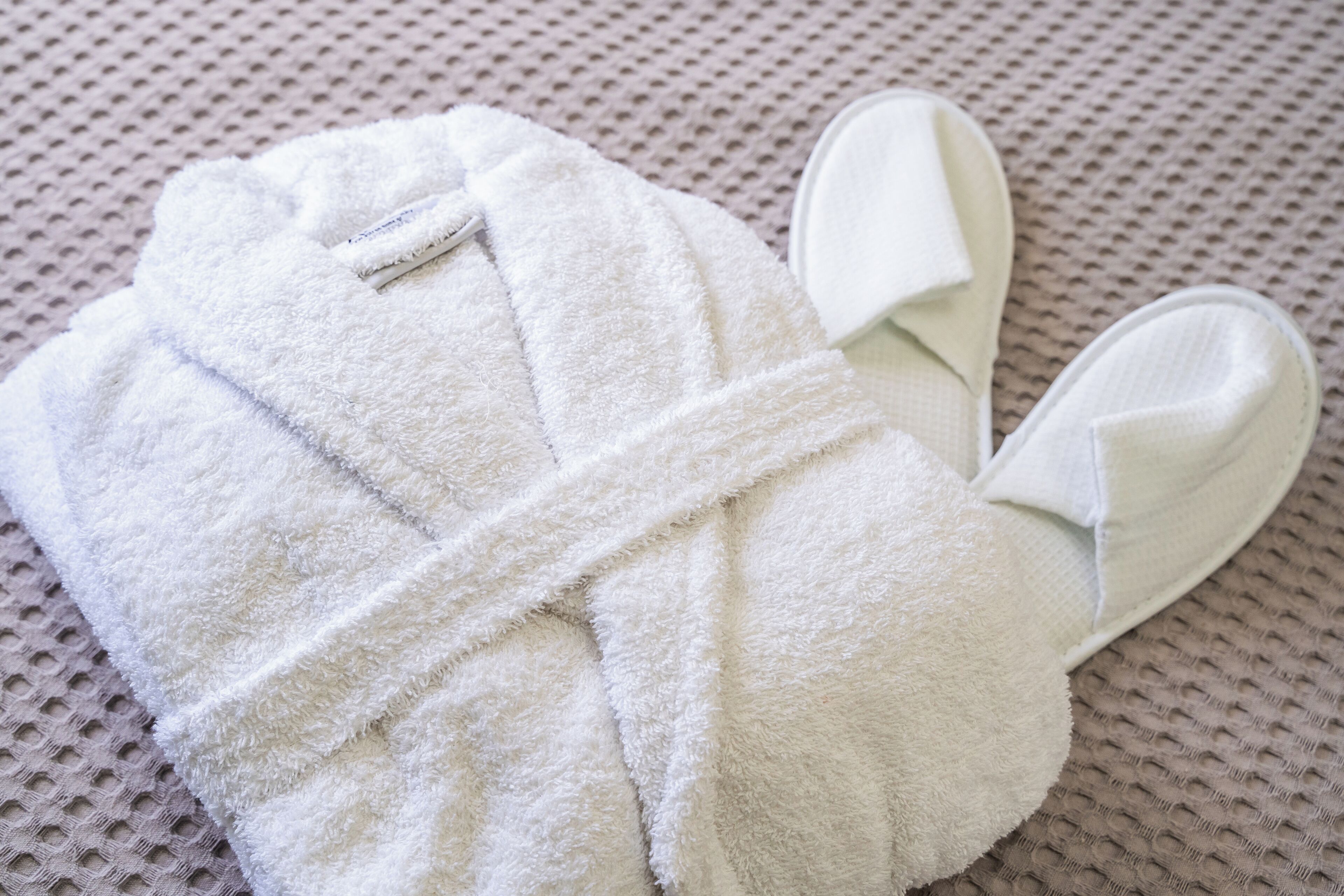 A white bathrobe and slippers on a textured surface.
