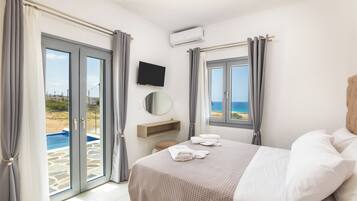 A bedroom with a bed, a TV, a view of the beach, and a pool.