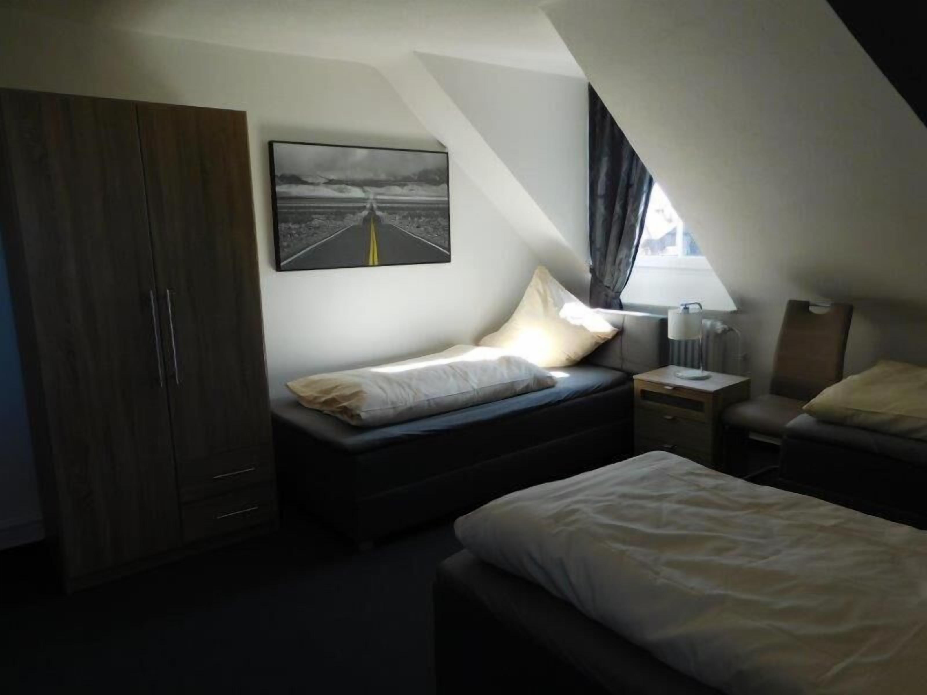 A small, dimly lit room with a single bed, a bedside table, a nightstand, and a wardrobe.