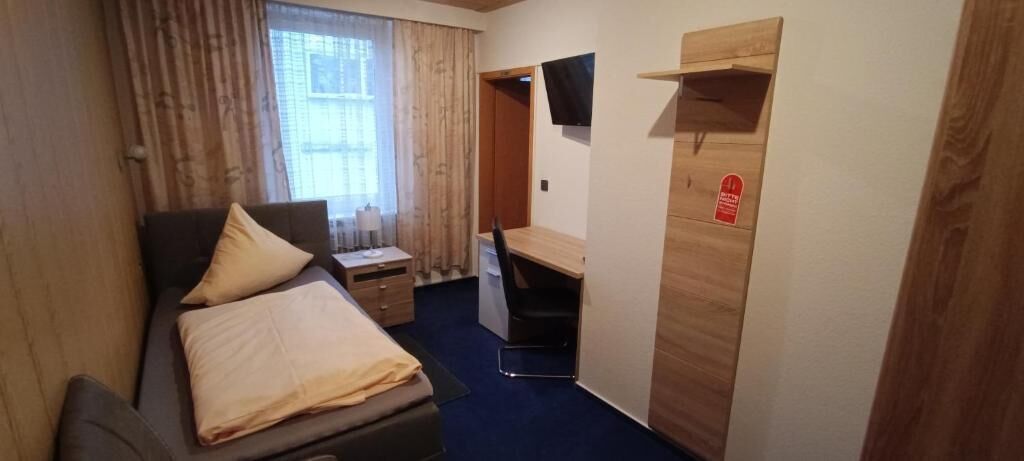 Una habitación pequeña con cama, escritorio, silla y televisor.