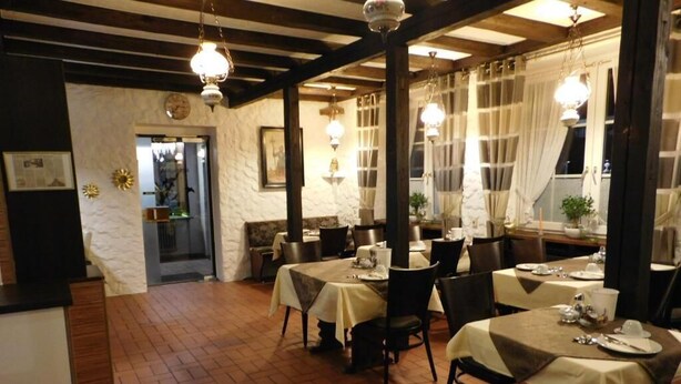 Un ristorante con pavimento in mattoni, tavoli apparecchiati con tovaglie bianche e sedie, e lampade pendenti.