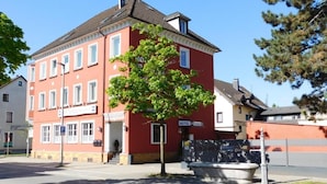 Un edificio rosso con un cartello che indica che si tratta di un hotel. C'è un albero di fronte all'edificio e una strada sullo sfondo.