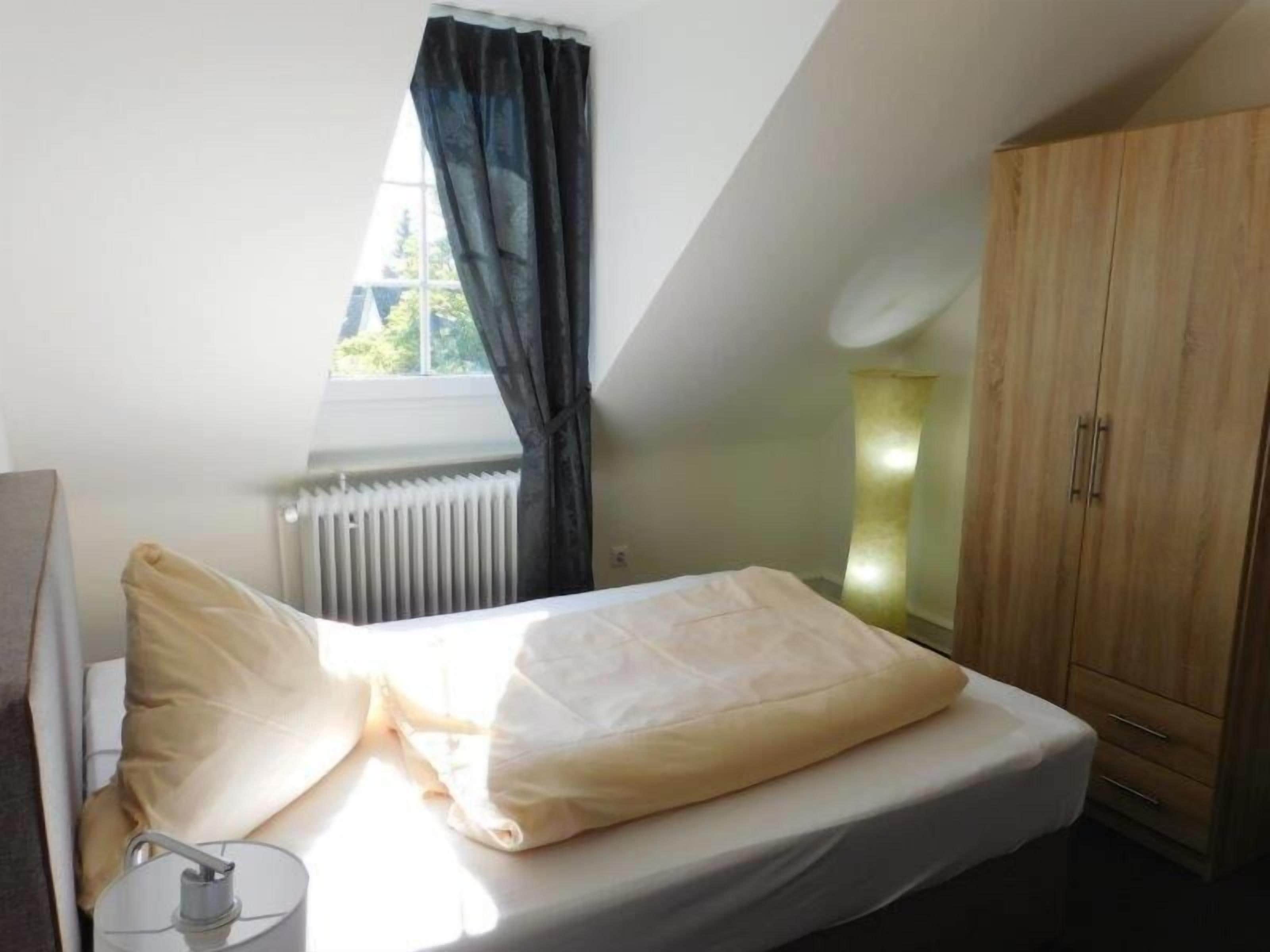 A bedroom with a bed, a radiator, a window with curtains, and a wardrobe.