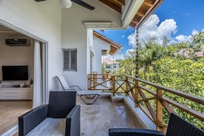 A balcony with wicker furniture, a TV, and a view of a lush garden. - Luxury 3-bedroom duplex with air-conditioning • Range 5 min (Las Terrenas)