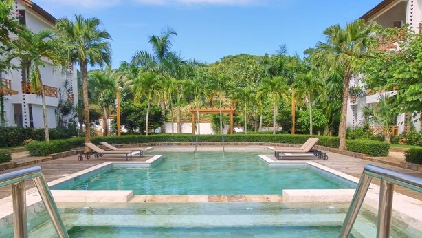 Une piscine au sol carrelé, entourée de palmiers et agrémentée d’une pergola.