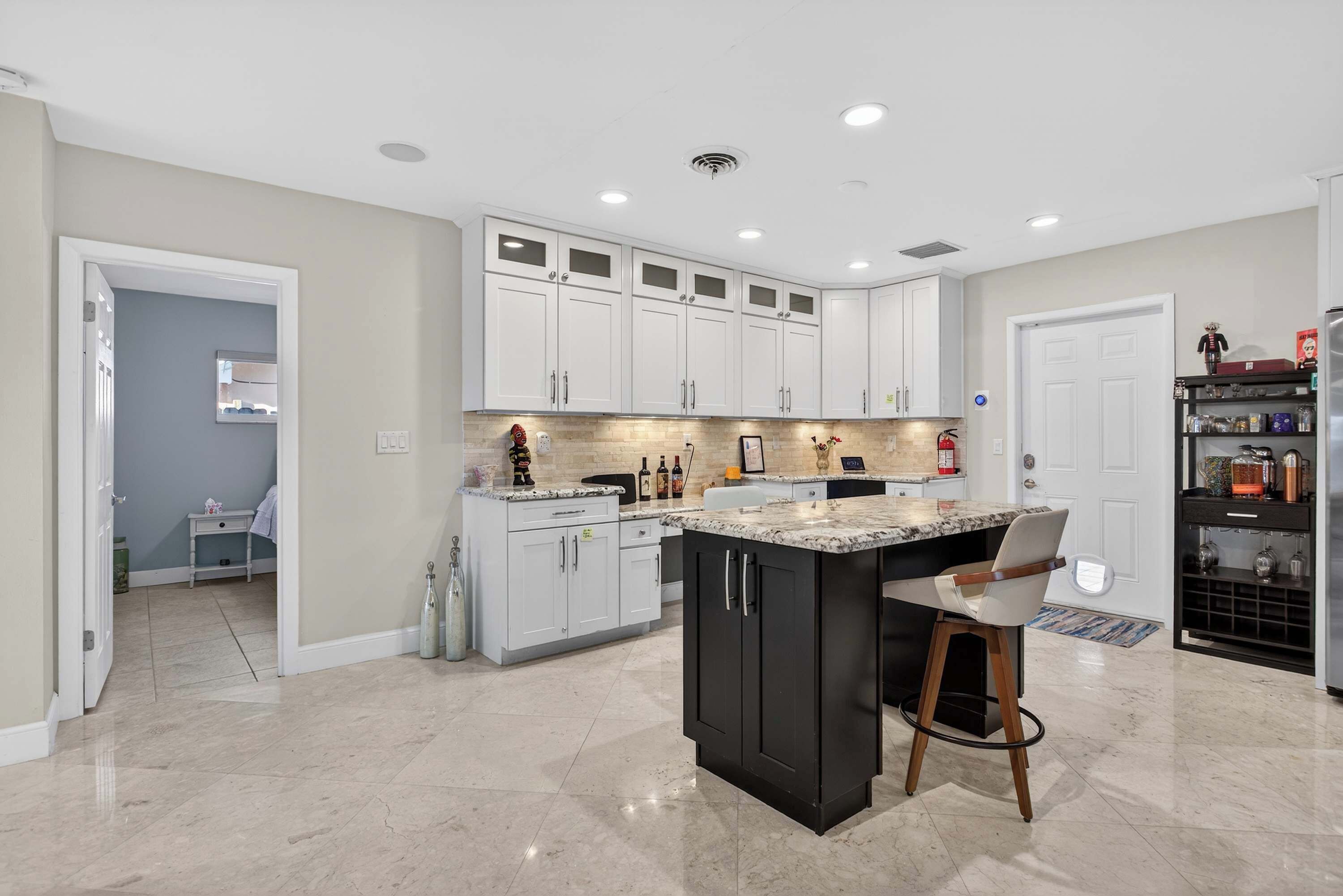 A modern kitchen with white cabinets, a black island, and a marble countertop.