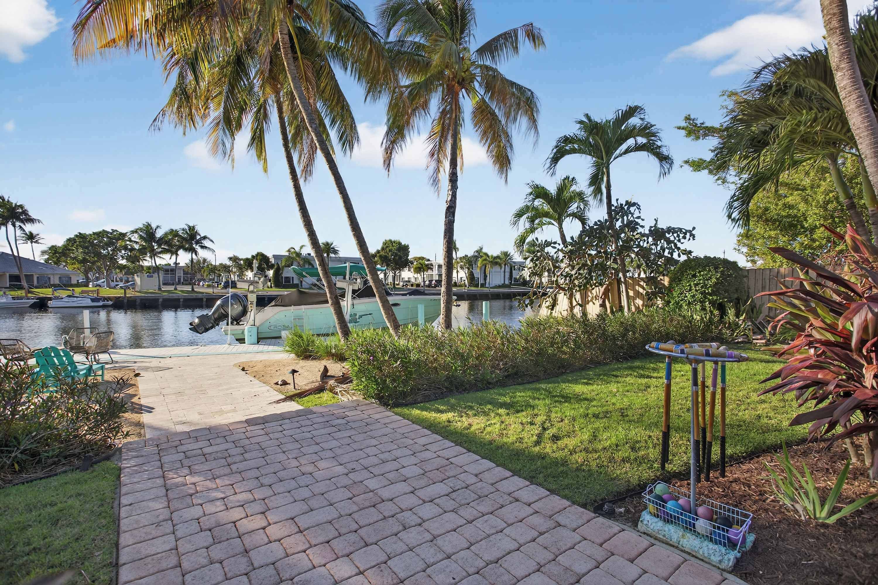 A paved pathway leading to a water body, surrounded by palm trees and greenery.