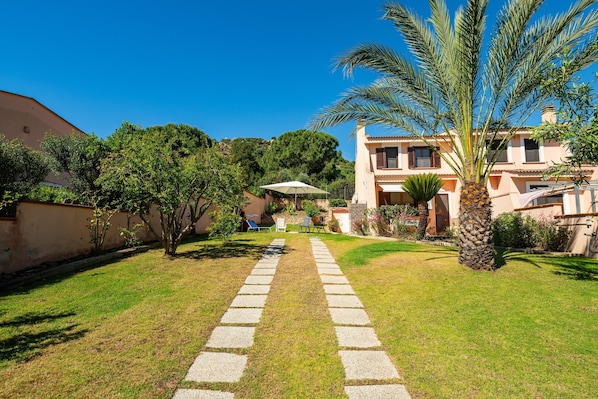 A pathway leading to a building with a garden, palm trees, and a clear blue sky.