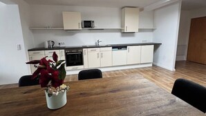 A modern kitchen with white cabinets, a microwave, and a coffee maker. There is a dining table with chairs and a vase of flowers. - Freshly renovated and large bright apartment in Löhne (Löhne)