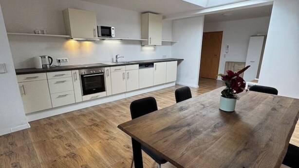 A modern kitchen with white cabinets, a wooden dining table, and a potted plant. - Freshly renovated and large bright apartment in Löhne (Löhne)