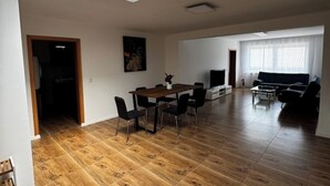 A spacious living room with a wooden floor, a dining area with a table and chairs, a sofa, and a TV. - Freshly renovated and large bright apartment in Löhne (Löhne)