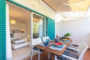 Une terrasse ouverte avec une table à manger, des chaises et un coin cuisine visible à travers les portes coulissantes.