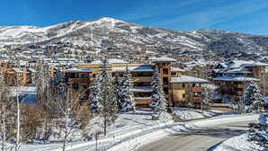 Un pueblo cubierto de nieve con edificios de varios pisos, una pista de esquí y un cielo azul despejado.