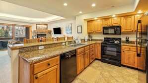 Una cocina moderna con encimeras de granito, armarios de madera y electrodomésticos de acero inoxidable, incluyendo un horno empotrado.