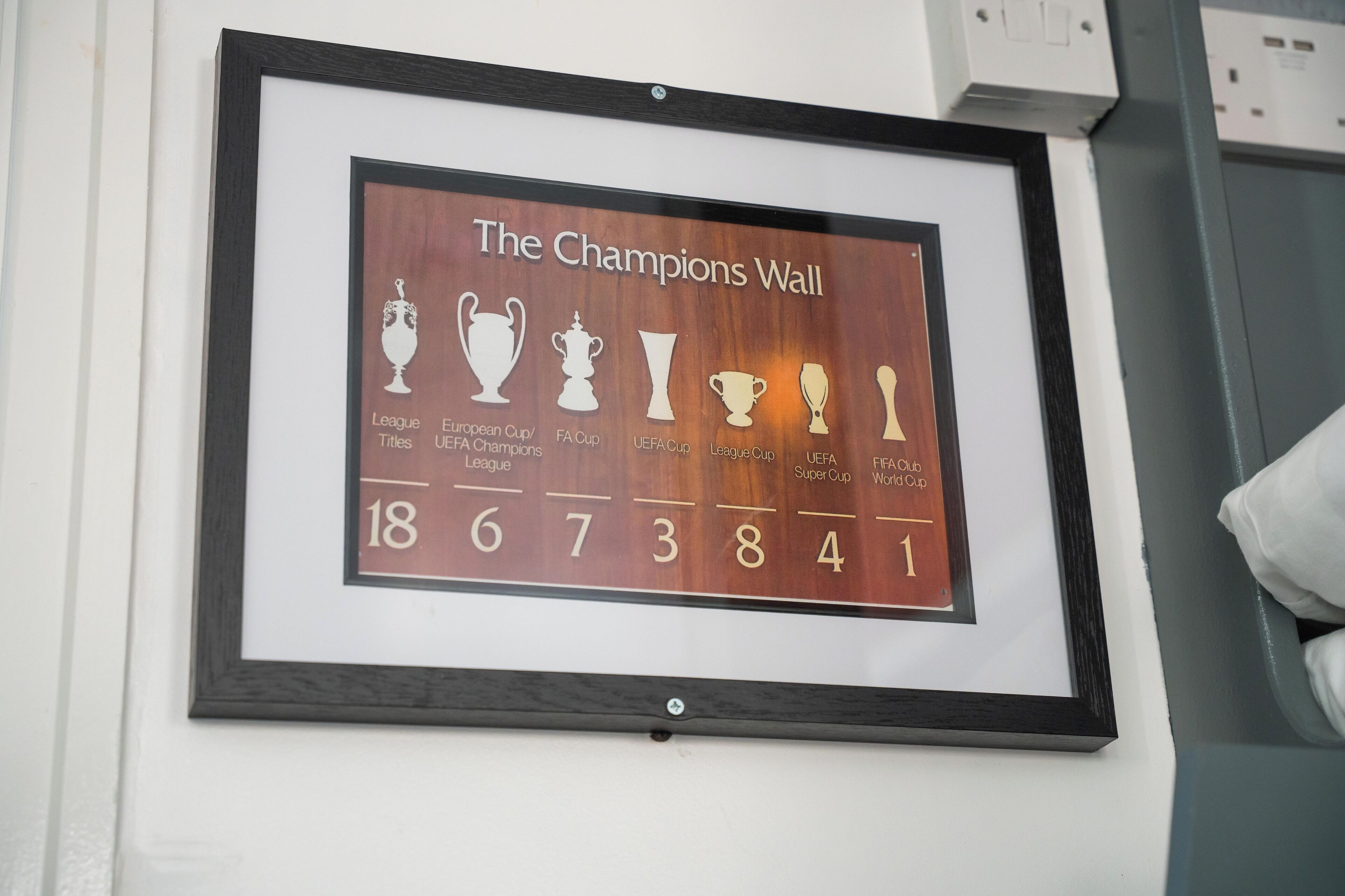 A framed display titled "The Champions Wall" with trophies and numbers representing various football championships.