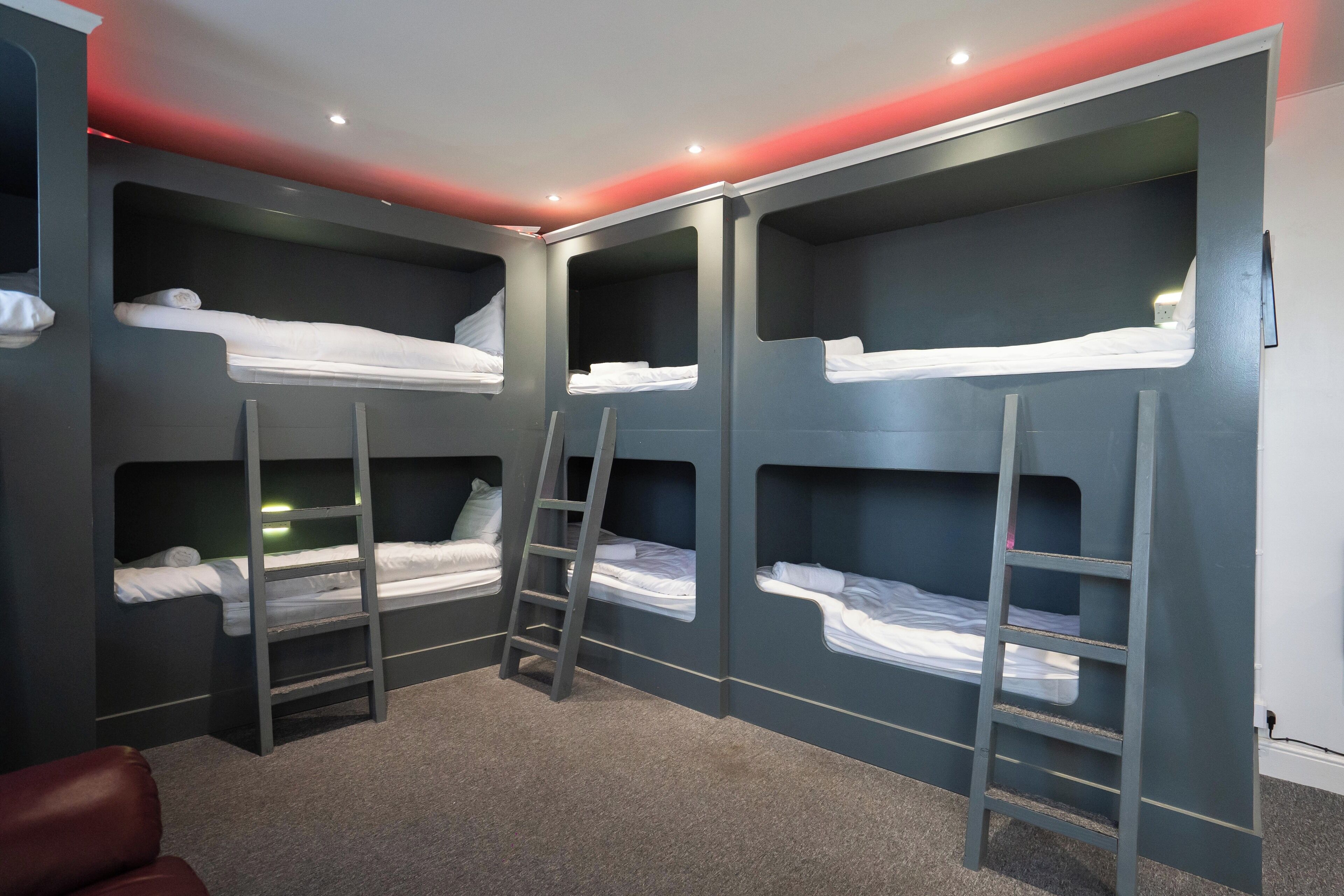 A room with bunk beds, a ladder, and a red-lit ceiling.