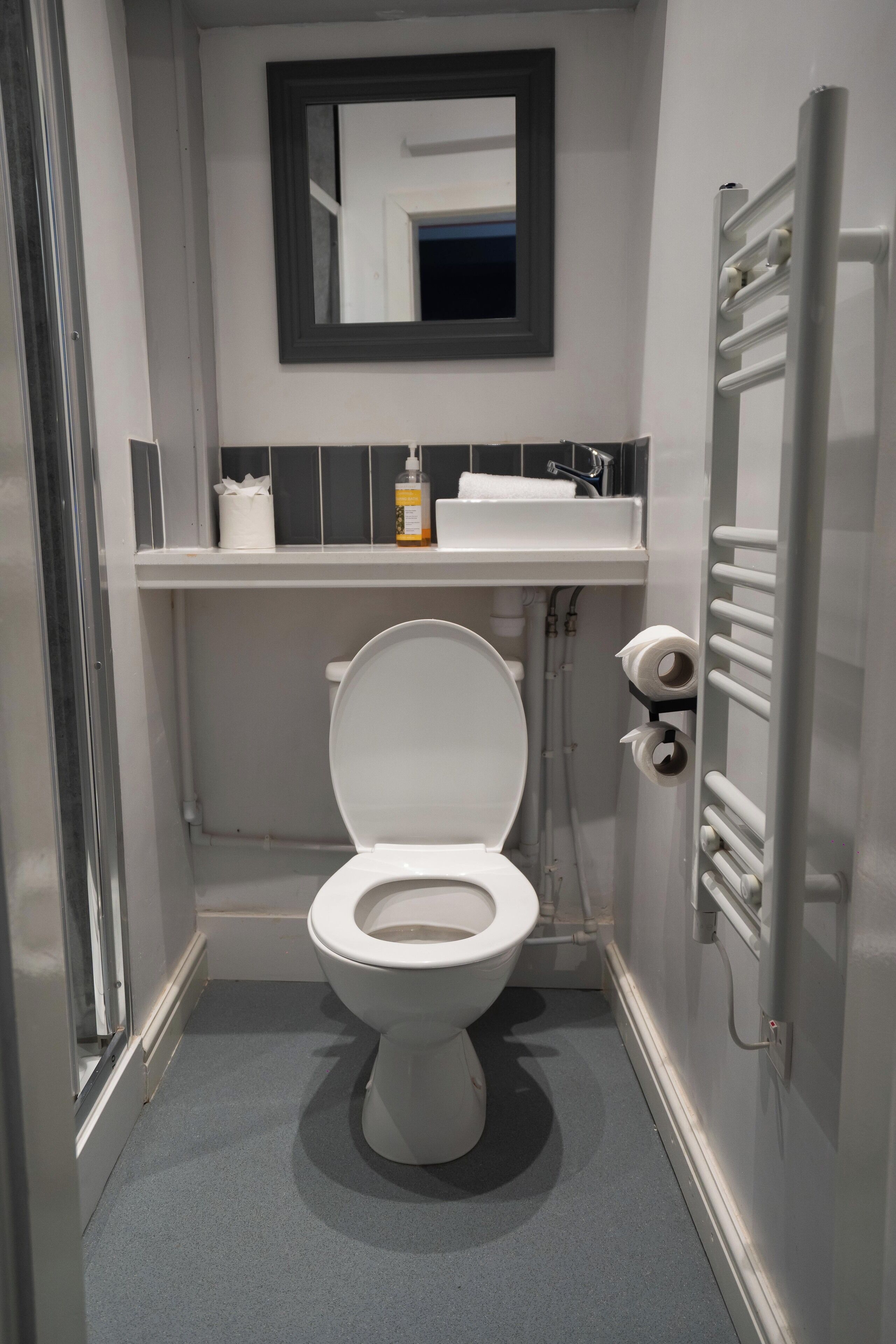 A compact bathroom with a white toilet, a mirror above the sink, and a towel dispenser.