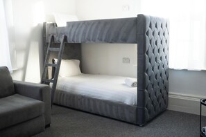 A bunk bed with a ladder, a grey armchair, and a small table with a cup. - The Breckfield Hotel (Liverpool)