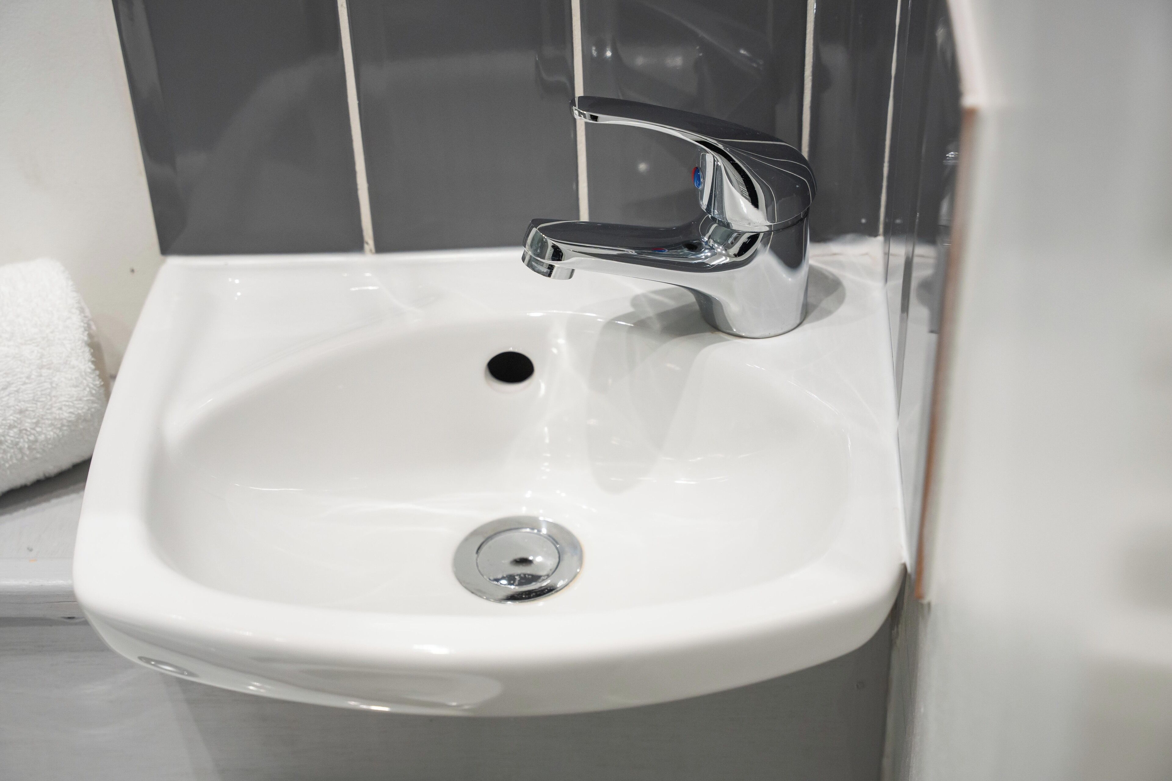 A white bathroom sink with a chrome faucet and a drain.