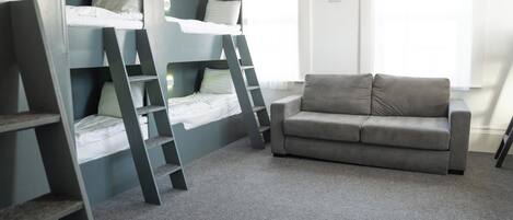 A room with bunk beds, a gray sofa, and a window with curtains.