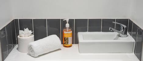 Ein Badezimmer mit einem weißen Waschbecken, einer Seifenflasche, einem weißen Handtuch und einer Toilettenpapierrolle.