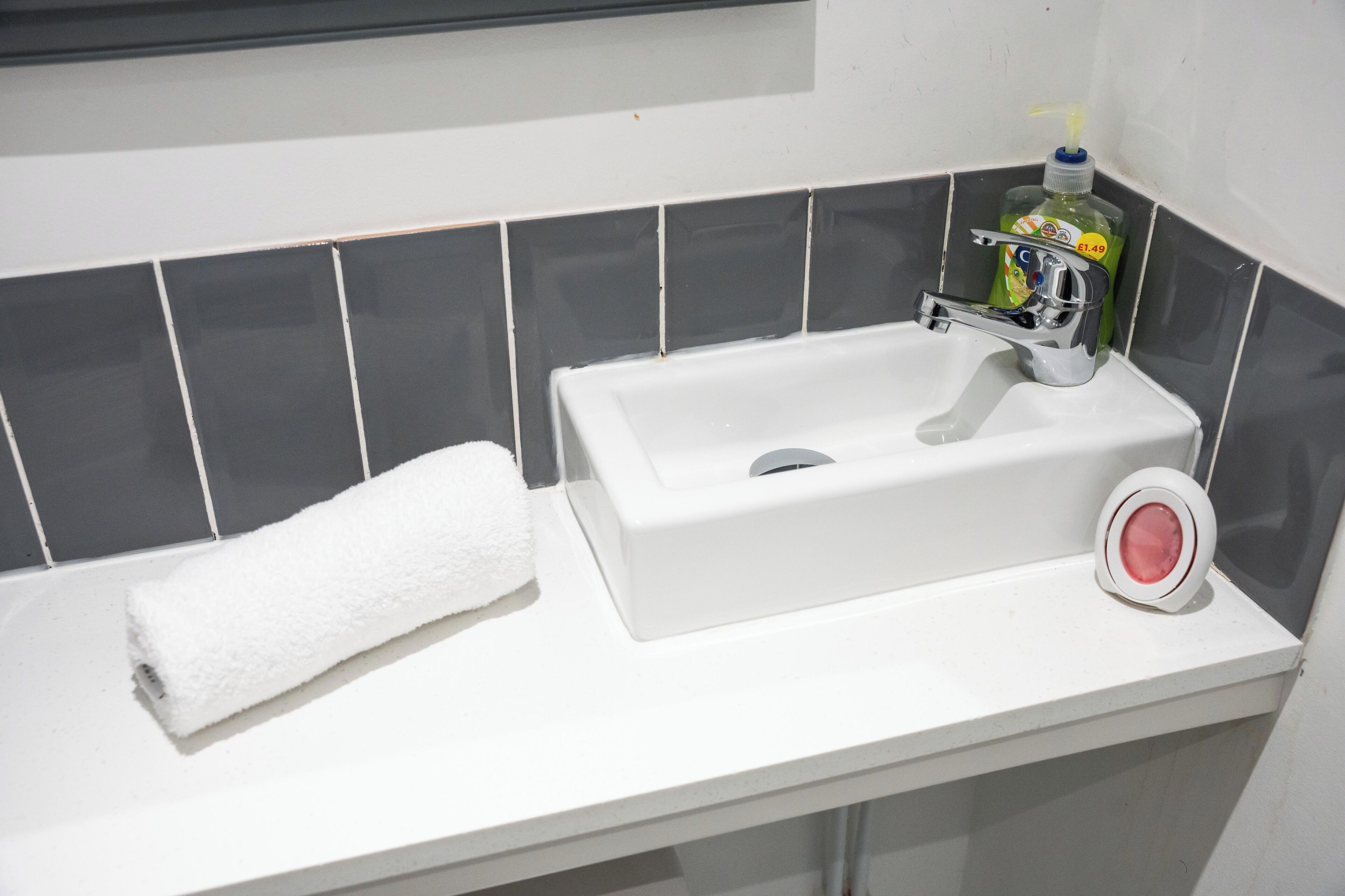 Une salle de bain avec un lavabo blanc, une serviette blanche et une bouteille de savon liquide vert.