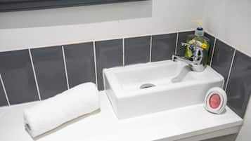 Une salle de bain avec un lavabo blanc, une serviette blanche et une bouteille de savon liquide vert.