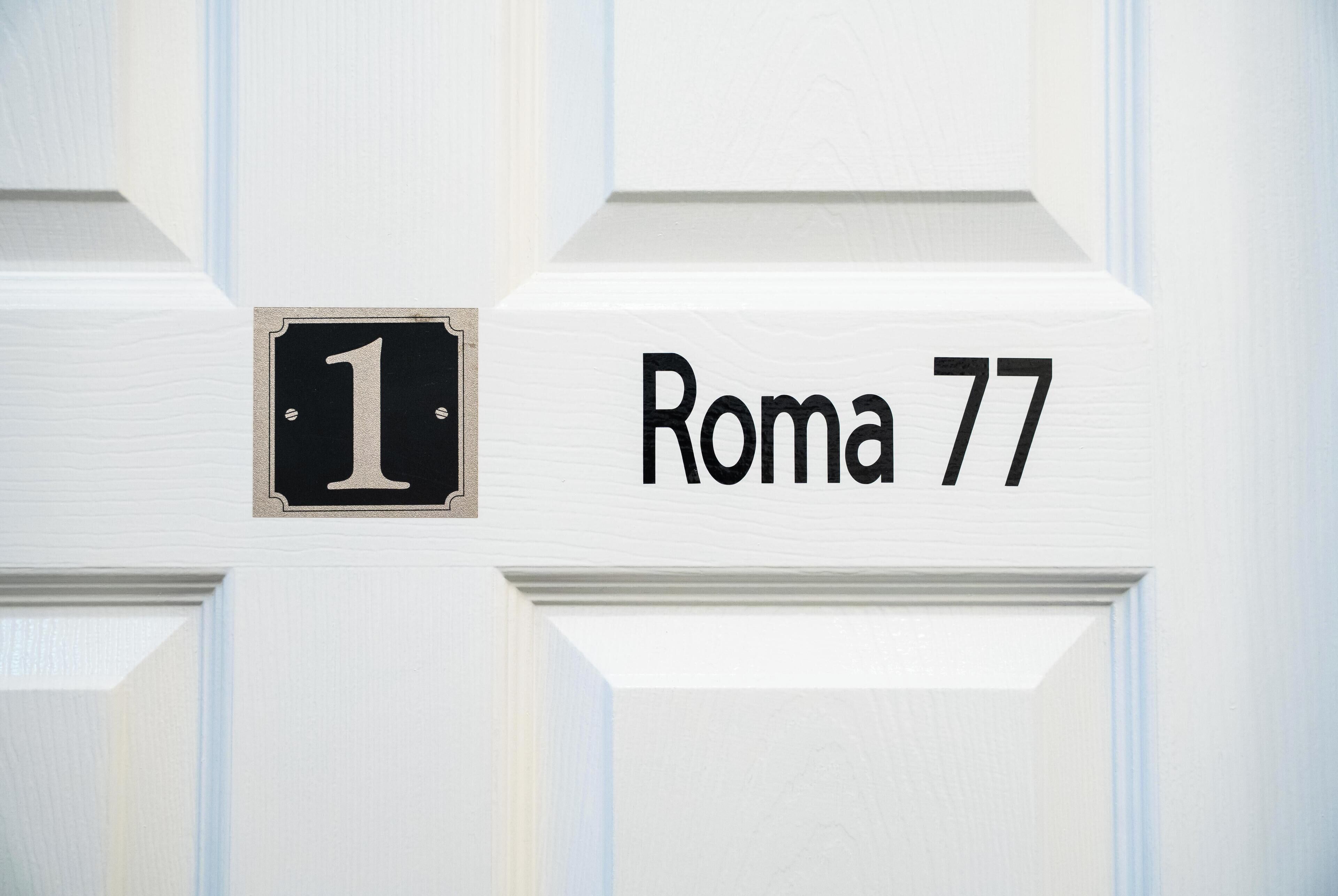 Una porta blanca amb una placa negra on hi posa el número '1' i el text 'Roma 77'.