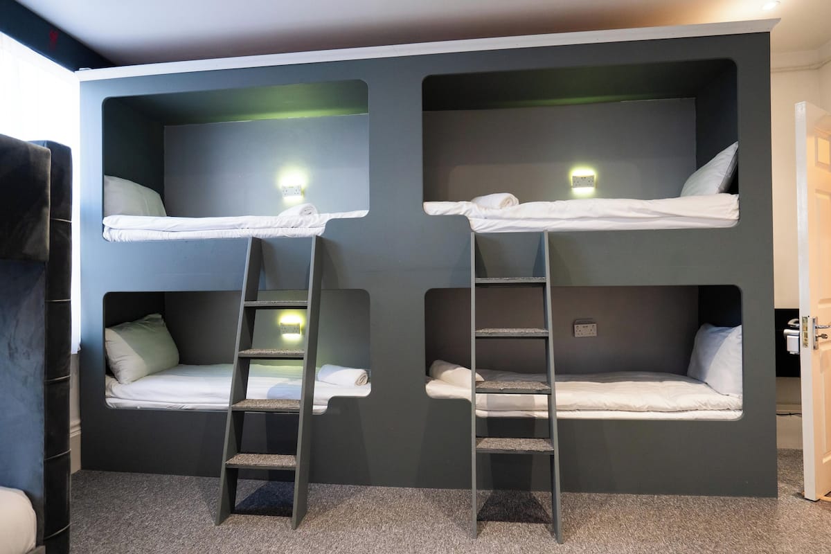 Una habitación con literas, cada una con una escalera, y un pequeño ventanal.
