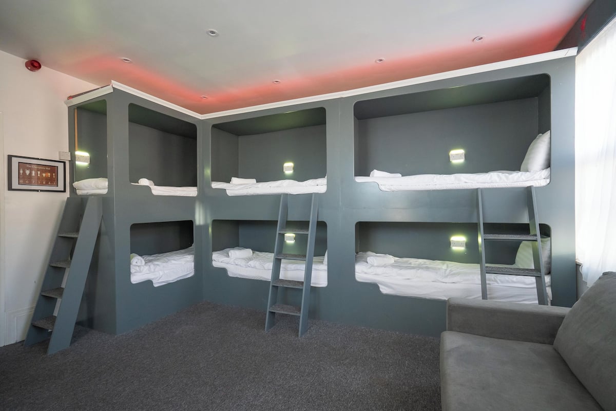 Una habitación con literas, una escalera, un sofá gris y un cuadro en la pared.