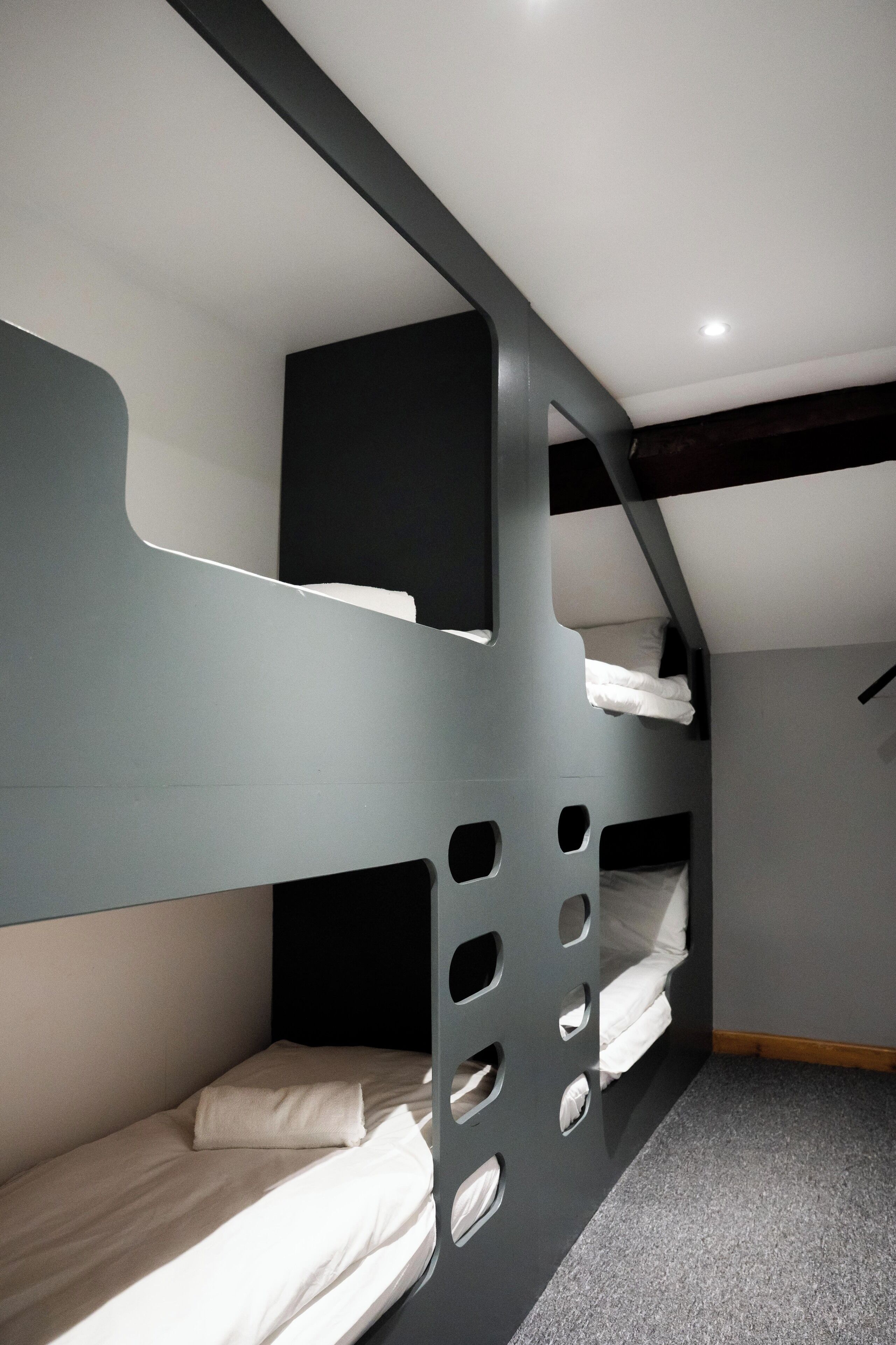 Ein Schlafraum mit Etagenbetten, grauer Wand und geneigter Decke.