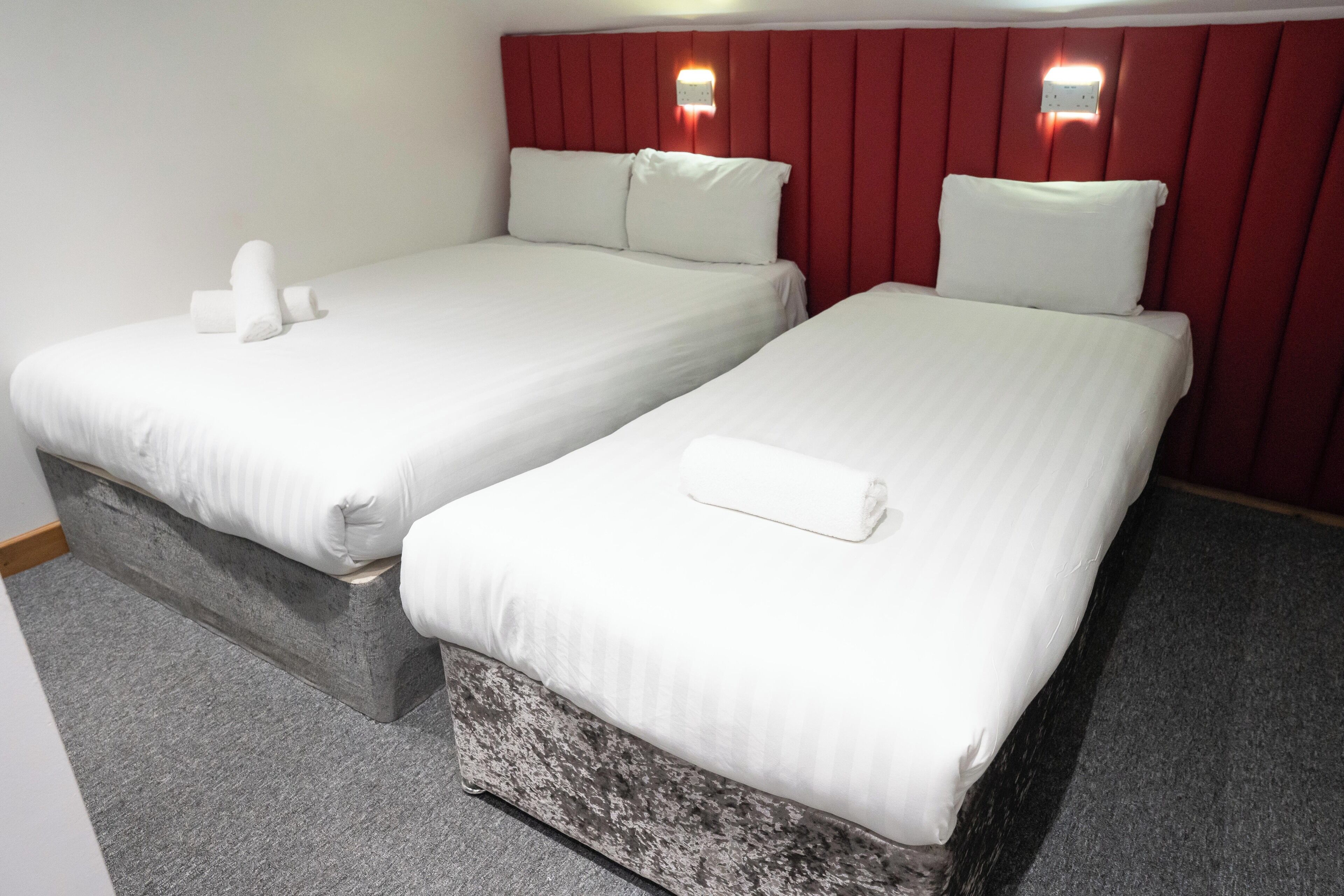 Two single beds with white linens and pillows, a red headboard, and a small wall-mounted light fixture.