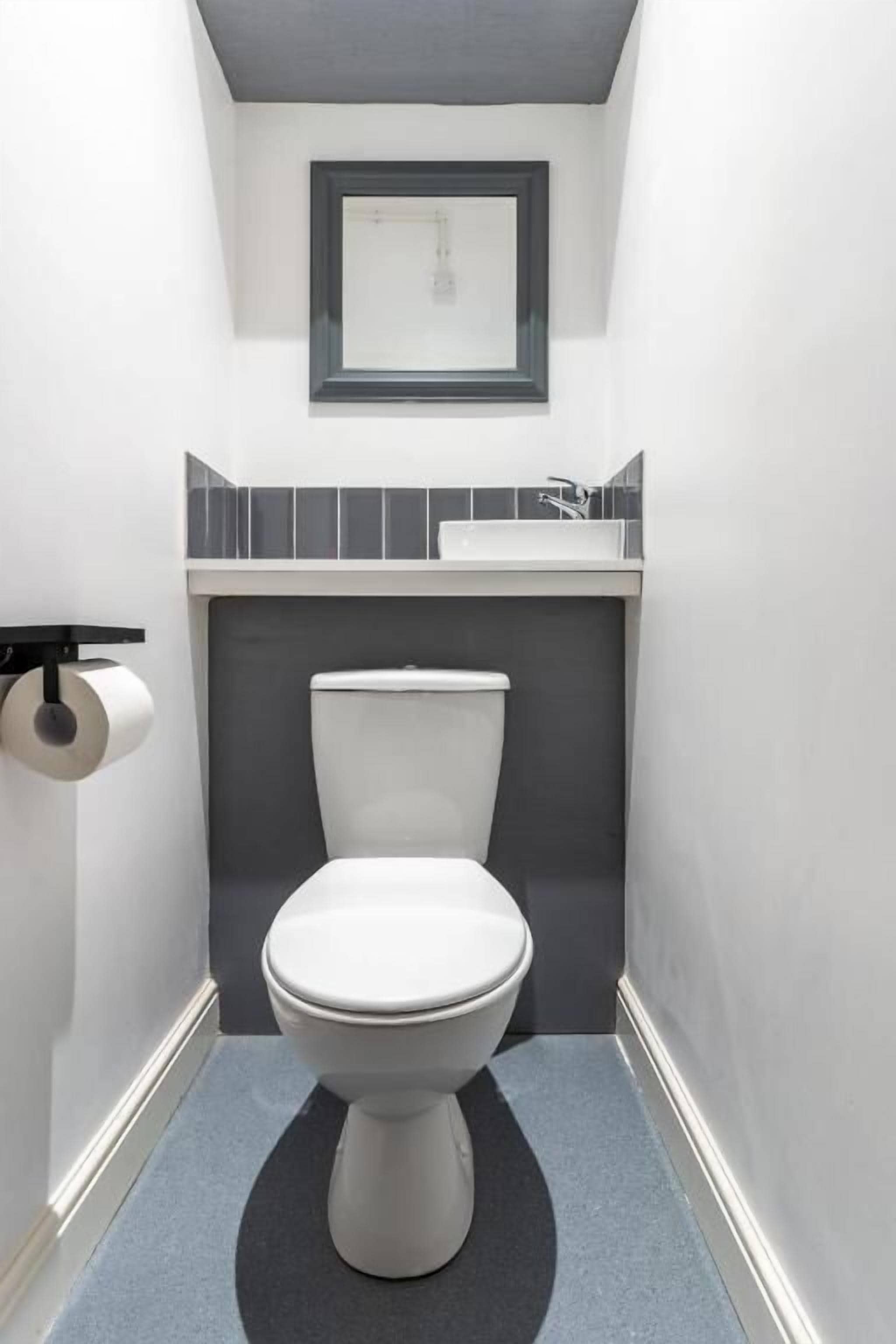 Une petite salle de bain moderne, équipée de toilettes, d’un lavabo et d’un miroir encadré au mur.